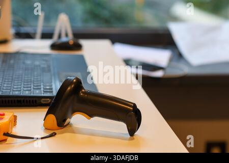 Lecteur de codes-barres portable noir et jaune reposant sur un bureau blanc près de l'ordinateur portable et de la souris Banque D'Images