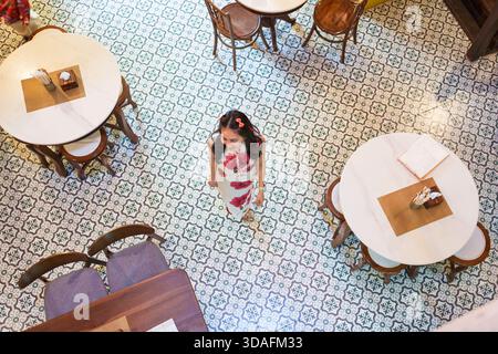 Vue aérienne d'une femme asiatique portant un cheongsam marchant dans un café chinois vintage avec carrelage à motifs, tables en marbre et chaises en bois Banque D'Images