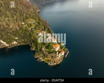 Vue aérienne d'une Villa del Balbianello historique avec des toits en terre cuite nichée sur une péninsule, contre des eaux bleues profondes et des collines verdoyantes, lac de Côme, L. Banque D'Images