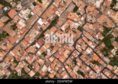 Vue aérienne des toits en terre cuite embrassés par le soleil et des rues labyrinthiques créent une tapisserie chaleureuse et texturée sur la ville antique, Taormina, Sicile, Italie. Banque D'Images