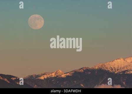 Vue aérienne d'une pleine lune suspendue au-dessus des sommets enneigés des montagnes Low Tatras, touchée par la lueur chaude du soleil couchant, Low Ta Banque D'Images