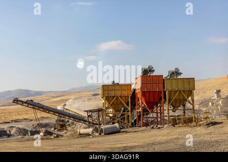 Usine de concassage de pierres et de production de gravier avec bandes transporteuses et trémies fonctionnant dans une carrière poussiéreuse à ciel ouvert par une journée ensoleillée. Banque D'Images