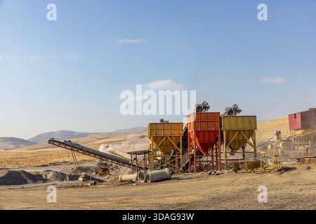 Usine de concassage de pierres et de production de gravier avec bandes transporteuses et trémies fonctionnant dans une carrière poussiéreuse à ciel ouvert par une journée ensoleillée. Banque D'Images