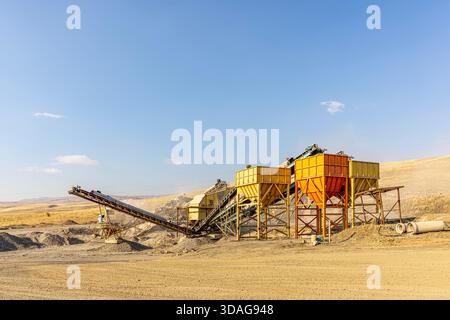 Usine de concassage de pierres et de production de gravier avec bandes transporteuses et trémies fonctionnant dans une carrière poussiéreuse à ciel ouvert par une journée ensoleillée. Banque D'Images