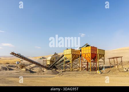 Usine de concassage de pierres et de production de gravier avec bandes transporteuses et trémies fonctionnant dans une carrière poussiéreuse à ciel ouvert par une journée ensoleillée. Banque D'Images