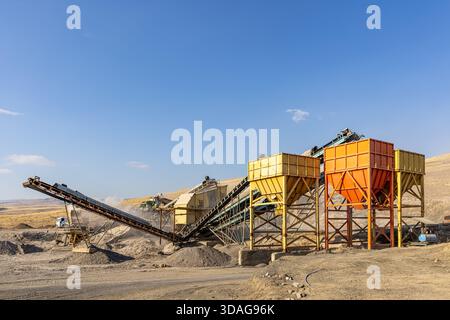 Usine de concassage de pierres et de production de gravier avec bandes transporteuses et trémies fonctionnant dans une carrière poussiéreuse à ciel ouvert par une journée ensoleillée. Banque D'Images
