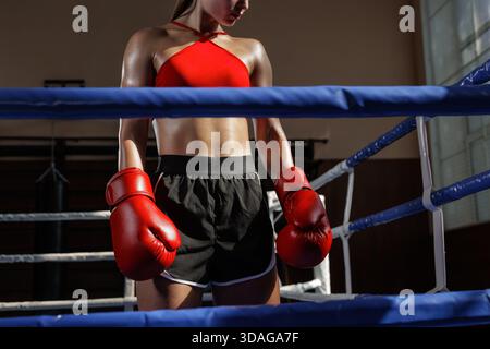 Athlète féminine forte dans un ring de boxe avec des gants rouges et un haut de sport prêt pour l'entraînement et la compétition Banque D'Images