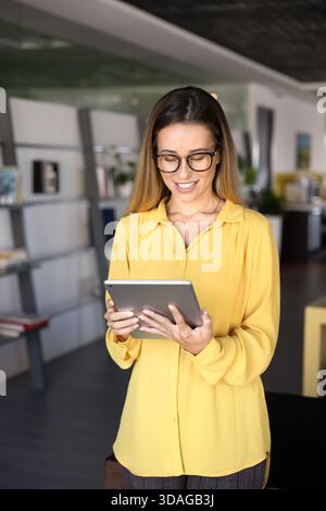 Jeune femme entrepreneure positive dans des lunettes élégantes à l'aide d'une tablette Banque D'Images