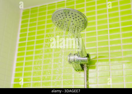L'eau coule d'une pomme de douche au-dessus des murs carrelés verts dans une salle de bains. La scène dispose d'un espace de copie suffisant pour le texte. Banque D'Images