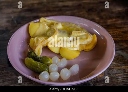 Fromage à raclette fondu sur pommes de terre bouillies, servi avec des oignons marinés et des concombres une spécialité suisse, le marché de Noël de Zurich, Suisse Banque D'Images