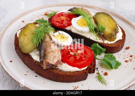 Sandwichs sur pain de seigle, avec sprats, œufs de caille, tomates fraîches et concombre mariné, apéritif, petit déjeuner, fait maison Banque D'Images