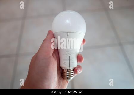 Gros plan de la main d'une personne tenant une ampoule LED défectueuse avec une grande fissure au milieu de l'ampoule au-dessus d'un sol carrelé dans une maison domestique, Lafayette, Californie, 18 juin 2025. (Photo Smith Collection/Gado/Sipa USA) Banque D'Images
