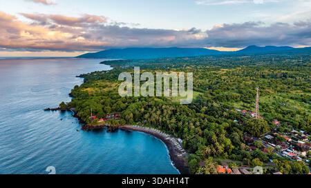 Vue aérienne drone de la côte de Tulamben à Bali au coucher du soleil avec montagnes et forêt Banque D'Images