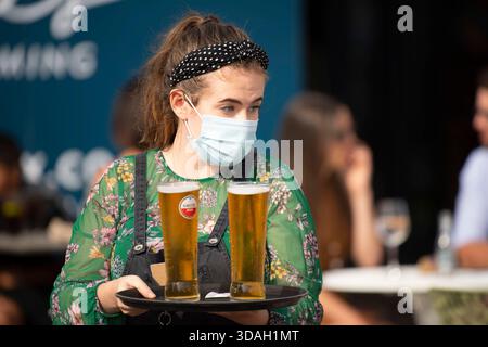 Une femme portant un masque facial sert deux pintes de bière pendant la pandémie de COVID-19 dans la baie de Cardiff, au pays de Galles. Banque D'Images