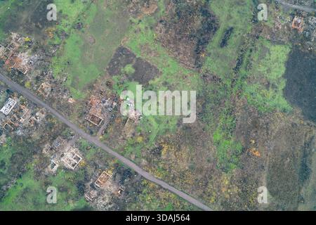 Vue de haut en bas des fondations de maisons dispersées et des ruines de bâtiments entourées d'une végétation verte dense et vibrante. Le contraste met en évidence la nature récupérant la colonie civile détruite dans une zone de guerre de l'Ukraine - tir de drone aérien Banque D'Images
