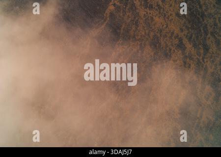 Texture de sol sombre et robuste partiellement obscurcie par une épaisse couche de brouillard blanc. Cette scène atmosphérique crée un motif de surface abstrait et mystérieux - tourné à partir d'un drone. Banque D'Images