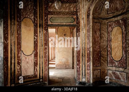 AGLIÈ, ITALIE – OCTOBRE 2025 : vue intérieure du château d'Agliè montrant des murs peints ornés, des textures de marbre vieilli et des portes menant à un corrido ensoleillé Banque D'Images