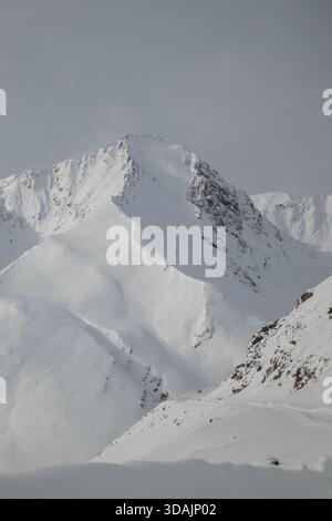 Vue rapprochée d'une crête montagneuse abrupte complètement recouverte de neige contre un ciel gris Banque D'Images
