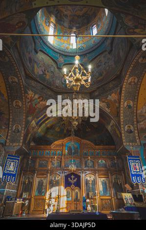 Petroșani, Roumanie 22 novembre 2025 : église orthodoxe intérieur iconostase en bois lustres dorés fresques colorées arches et dôme lumière naturelle Banque D'Images