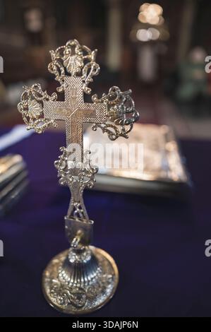 Petrosani, Roumanie 22 novembre 2025 : croix d'argent ornée sur un stand en tissu liturgique violet profond relié à l'argent livre religieux flou fond Banque D'Images