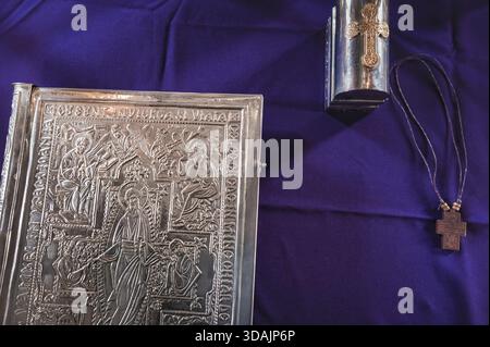 Petrosani, Roumanie 22 novembre 2025 : livre gospel orné relié en argent collier croix en bois chrism boîte objets rituels en tissu liturgique violet profond Banque D'Images