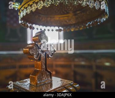 Petrosani, Roumanie 22 novembre 2025 : support orné d'une croix en bois étincelante illuminé par la lumière d'un lustre doré de fenêtre dans une église orthodoxe Banque D'Images