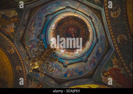Petrosani, Roumanie 22 novembre 2025 : vue à angle bas d'un dôme d'église orthodoxe et fresques de plafond illuminées par des fenêtres. Banque D'Images