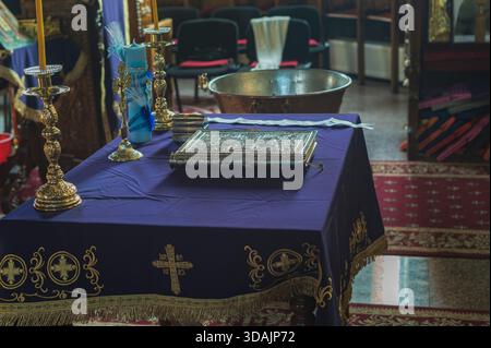Petroșani, Roumanie, 22 novembre 2025 : table avec une broderie de croix en tissu violet, livre gospel à reliure argentée et chandeliers dorés dans une église Banque D'Images