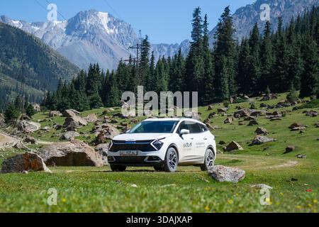 Région de Naryn, Kirghizistan - 13 mai 2024 : vue de face du vus blanc Kia Sportage garé sur une prairie verte avec des rochers dispersés et des montagnes enneigées Banque D'Images