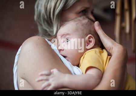 Une institutrice de crèche tient un bébé mignon contre sa poitrine, réconfortant et apaisant le nouveau-né à la garderie pendant la journée. Le bébé a l'air ALE Banque D'Images