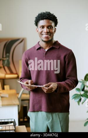Portrait d'un jeune homme noir adulte souriant tout en tenant des documents à l'intérieur Banque D'Images