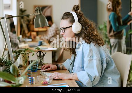 Jeune femme caucasienne portant des écouteurs travaillant sur l'ordinateur dans le bureau Banque D'Images