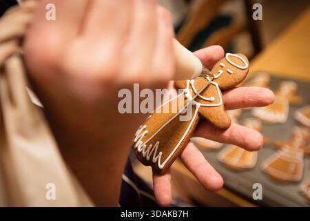 Gros plan d'une main tapissant du glaçage blanc sur un biscuit au pain d'épices. Banque D'Images