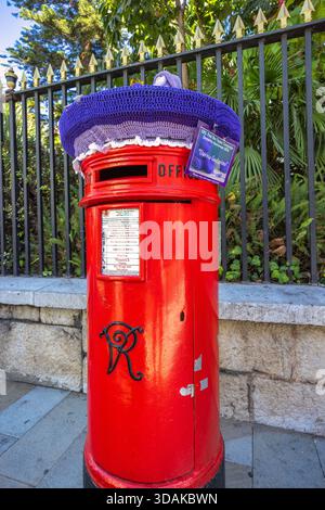 Gibraltar, Royaume-Uni - 10 septembre 2024 : boîte postale victorienne de conception britannique standard. Une boîte postale rouge ornée d'un mauve et lavande tricoté à la main Banque D'Images