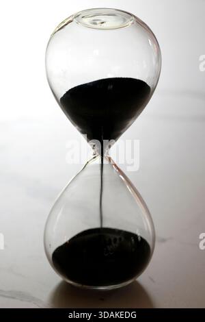 Un seul sablier rempli de sable noir symbolise le passage irréversible du temps et la mortalité humaine. Banque D'Images