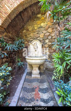 Malaga, Espagne - 11 septembre 2024 : Alcazaba, palais et fortification. Fontaine en pierre nichée dans une cour luxuriante, entourée de briques et de murs de pierre Banque D'Images