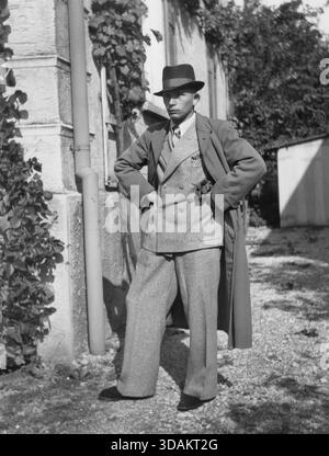 Un homme porte un costume de flanelle, un manteau et un chapeau. [traduction automatique] Banque D'Images