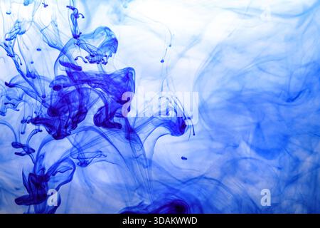 Encre bleue injectée dans l'eau à partir de la seringue, mélange de couleurs avec de l'eau créant des formes abstraites Banque D'Images