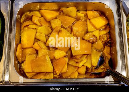 Une vue rapprochée de dés de courges jaunes enrobés d'une sauce sucrée étincelante, prête à être servie dans un plat froissé Banque D'Images