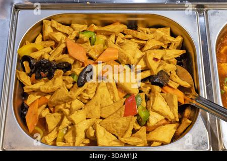 Une vue rapprochée d'un plat de frottement en métal fumant rempli de morceaux de tofu doré frits mélangés à des carottes vibrantes, des poivrons et des champignons noirs. Banque D'Images