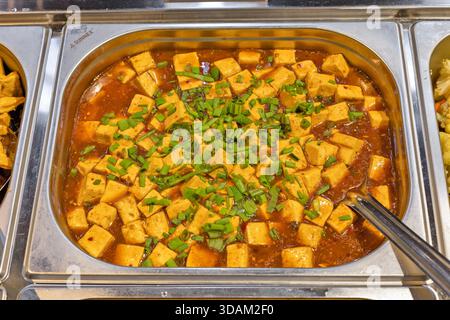 Une vue rapprochée d'un savoureux plat de tofu mapo, une cuisine populaire du Sichuan, présenté dans un grand plateau de service en métal, prêt à être apprécié par les convives Banque D'Images