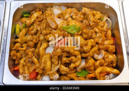 Une vue rapprochée d'un plat salé avec des morceaux de poulet frits croustillants enrobés d'une sauce aigre-douce brillante, mélangés à des légumes colorés Banque D'Images