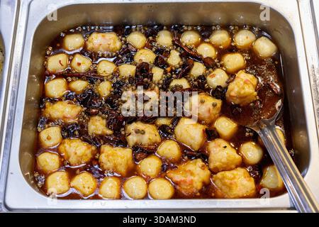 Vue rapprochée d'un plateau en métal fumant rempli de morceaux de poisson tendres et de petites boules de tofu immergées dans un riche bouillon épicé infusé de piment sec Banque D'Images