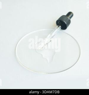 Compte-gouttes transparent avec sérum cosmétique sur boîte de Petri transparente sur fond blanc. Banque D'Images