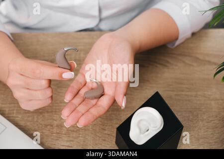 Les prothèses auditives numériques modernes dans les mains de l'audiologiste en clinique. Médecin tenant une prothèse auditive, modèle près de l'oreille pour l'ajustement et la démonstration. Gros plan, haut Banque D'Images