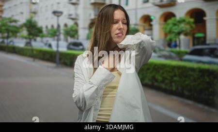 Femme tenant la gorge avec la main et touchant le cou sur la rue de la ville montrant étouffement et douleur à la gorge ; détresse. Banque D'Images