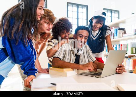 Groupe multiethnique de jeunes étudiants se réunissant à la bibliothèque - groupe multiethnique de jeunes étudiants souriants, collaborant sur un ordinateur portable pendant stu Banque D'Images