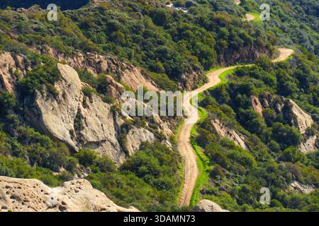 Des routes de terre pittoresques serpentent à travers des collines verdoyantes et des formations rocheuses de grès distinctives sous la lumière du soleil dans le paysage accidenté des Calabasas. Banque D'Images