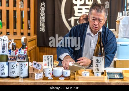 Un membre du personnel vêtu d’un happi traditionnel verse du namazake, du saké frais non pasteurisé, à Naikūmae Shuzōjō, la « brasserie devant le Sanctuaire intérieur » à Oharai-machi, Ise, préfecture de Mie, au Japon. La marque de saké Okage porte le nom de l’historique pèlerinage de masse Okagemairi, au cours duquel des millions de Japonais ont effectué des pèlerinages spontanés à Ise aux XVIIe et XVIIIe siècles. Le saké est une offrande centrale aux dieux dans le shintoïsme. Banque D'Images