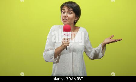 Femme tenant un microphone rouge et faisant des gestes la main ouverte tout en souriant et haussant les épaules contre un écran vert de studio ; livraison ludique spontanée. Banque D'Images